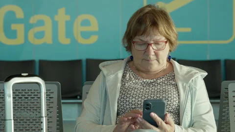 Senior woman uses smartphone while waiting at modern airport terminal gate Stock Footage 343950893