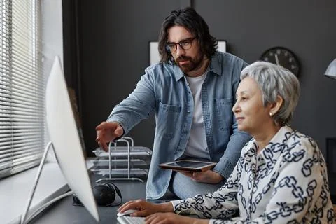 Senior woman using computer in class with male teacher helping Stockfoto's