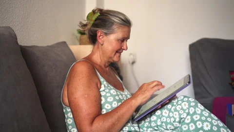 Senior woman using digital tablet on sofa at home Stock Footage 303855968
