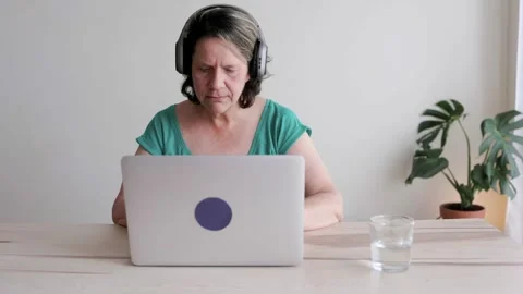 Senior woman using laptop computer while listening music or podcast at home Stock Footage 246944187