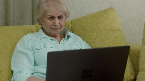 Senior woman using laptop computer on yellow sofa in comfortable home setting Stock Footage 322812959