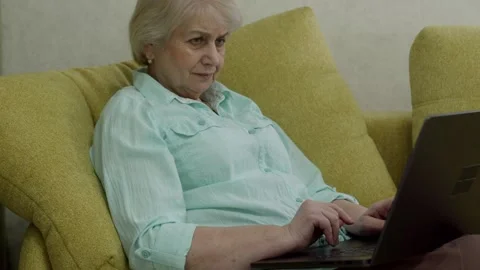 Senior woman using laptop while sitting on comfortable sofa Stock Footage 321856251