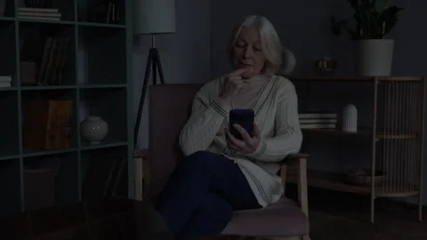 Senior Woman Using Smartphone During Power Outage In Dark Home Interior Stock Footage 334716513