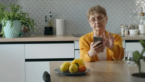 A senior woman using a smartphone while sitting in the kitchen Stock Footage 275023649