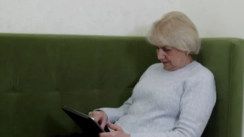 Senior woman using tablet while sitting on sofa at home Video stock 329244145