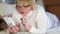 Senior woman with white smartphone lies on the bed HD Footage