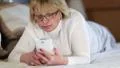 Senior woman with white smartphone lying on the bed and listening to music HD Footage