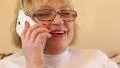 Senior woman with white smartphone speaks and gesticulate HD Footage