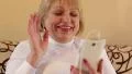Senior woman with white smartphone talks sits on the sofa HD Footage