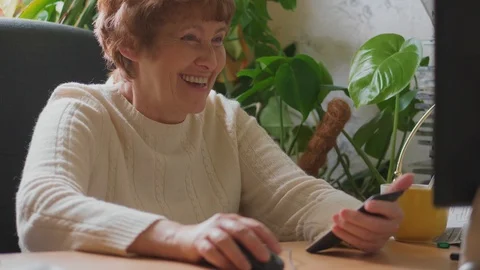 Senior woman working on computer, calling mobile, laughing Stock Footage 107558548