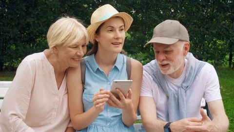 Seniors and daughter sit in park browse in mobile phone. Family look for Stock Footage