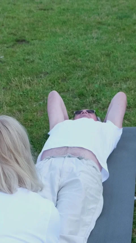 Seniors do abdominal exercises lying on the green grass in the park. Sports life Stock Footage 250384387