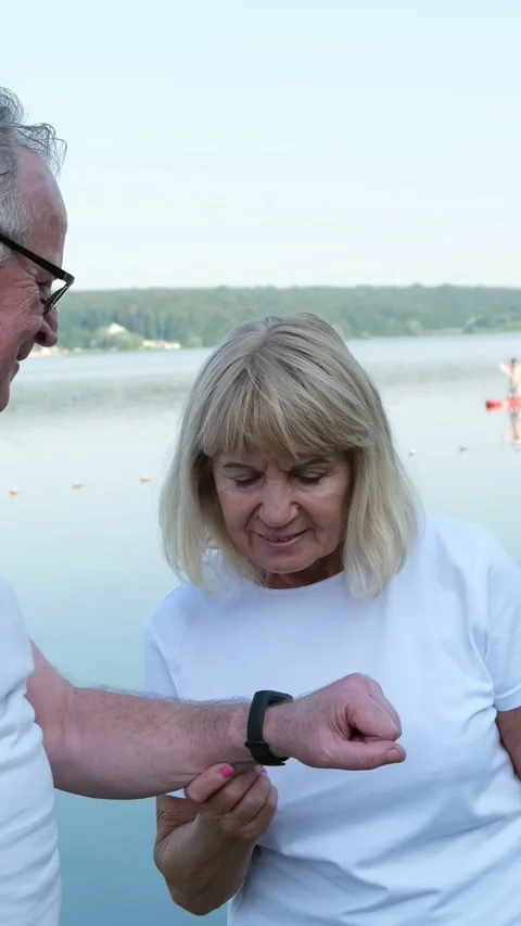Seniors talking by the lake using a smart watch. Sports training after Stock Footage 250381990