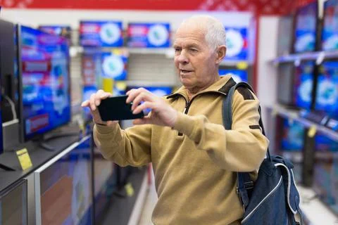 Senor man pensioner scanning QR code modern digital televisor with smart tv in Stock Photos
