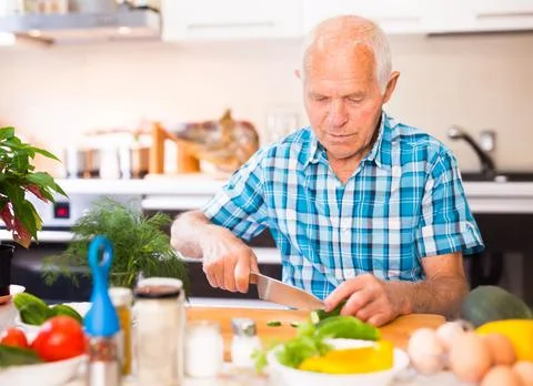 Senor man preparing fresh vegetable salad at home in the kitchen Stock Photos