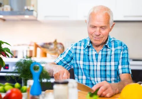 Senor man preparing fresh vegetable salad at home in the kitchen Stock Photos