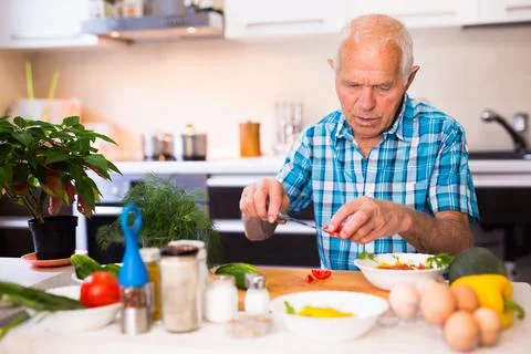 Senor man preparing fresh vegetable salad at home in the kitchen Stock Photos
