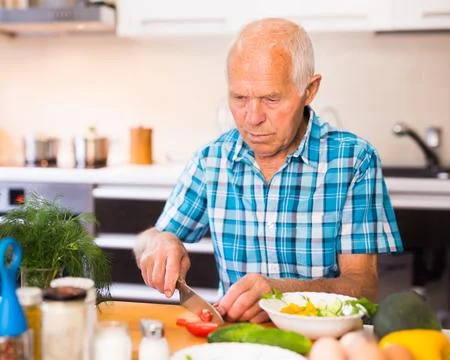 Senor man preparing fresh vegetable salad at home in the kitchen Stock-Fotos