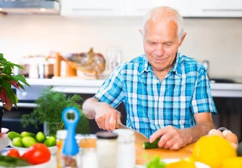 Senor man preparing fresh vegetable salad at home in the kitchen Stock Photos