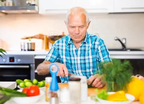 Senor man preparing fresh vegetable salad at home in the kitchen Foto stock