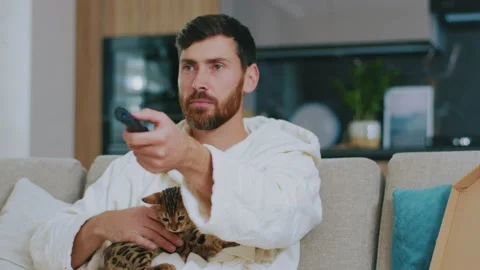 Sensitive man with cat watching TV. Sitting on sofa cry sad at home. Relaxation Stock Footage 143712985