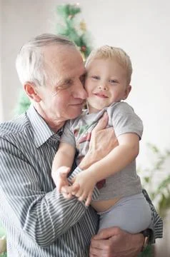 Sentimental old man holding a small child in his arms at Christmas in front of a Stock Photos