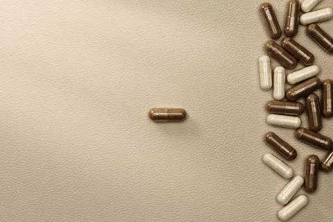 Separating brown and white supplement capsules on beige background Stock Photos