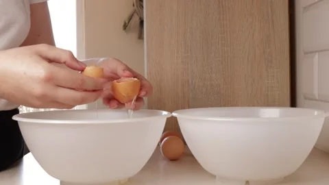 Separating chicken eggs into whites and yolks in a bright home kitchen, han.. Stock Footage 318672192