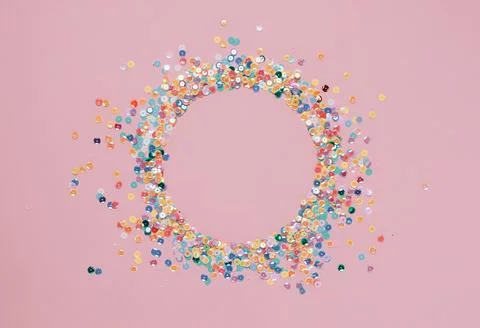 Sequins multicolored confetti lined in round frame pink background. Abstract Stock Photos