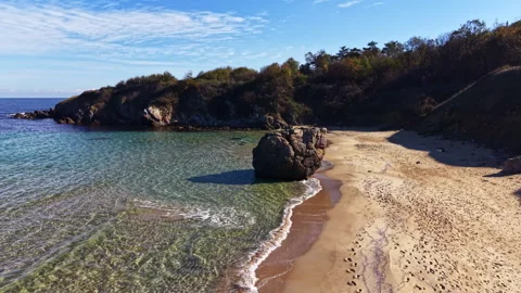 Serene beach with rocky outcrop and gentle waves under a clear blue sky in late Stock Footage 331256341