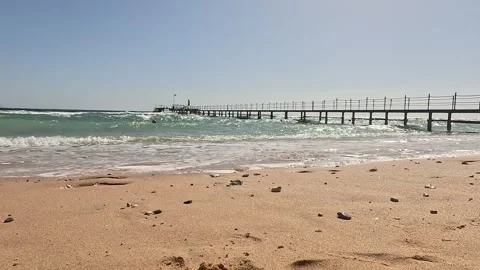 Serene Beach Scene Featuring Gentle Waves and a Pier on a Bright Sunny Day Video stock 330119416