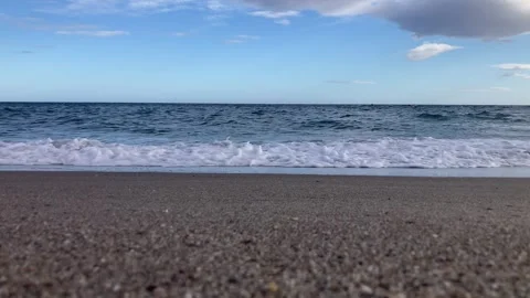 A serene beach scene with gentle waves rolling onto the sand under a blue sky Stock Footage 289448652