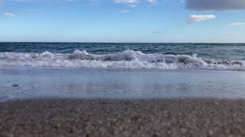 A serene beach scene with gentle waves rolling onto the sand under a blue sky Stock Footage 289448653