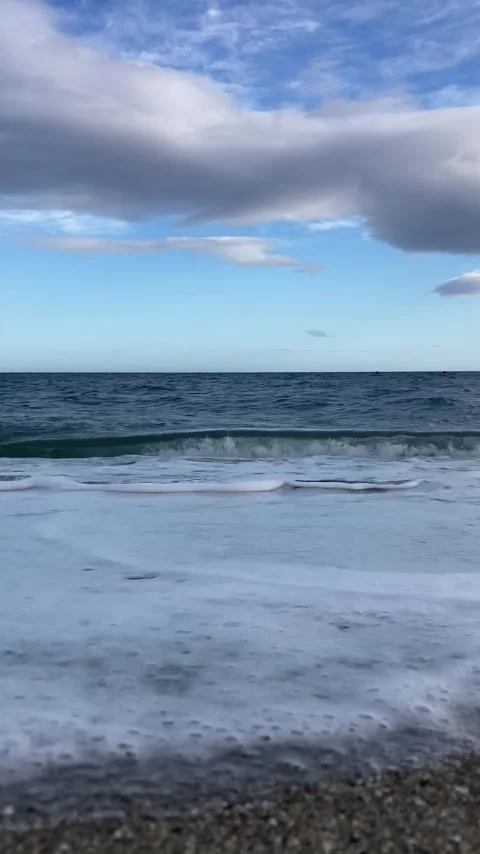 A serene beach scene with gentle waves rolling onto the sand under a blue sky Stock Footage 289448657