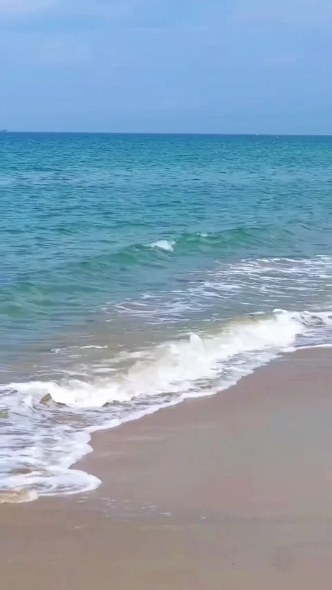 A serene beach scene with gentle waves lapping at the shore on a sunny day in a Stockbeeldmateriaal 333021820
