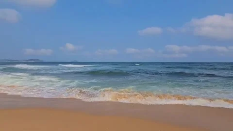 A serene beach scene with gentle waves lapping at the shore under a clear blue Stockbeeldmateriaal 333022111