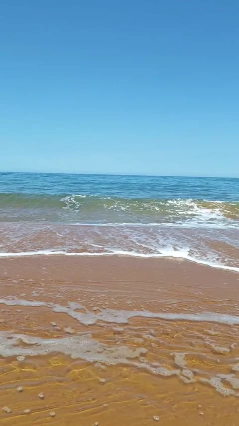 Serene beach scene with ocean waves crashing on golden sand under clear blue sky Vidéo 334084967