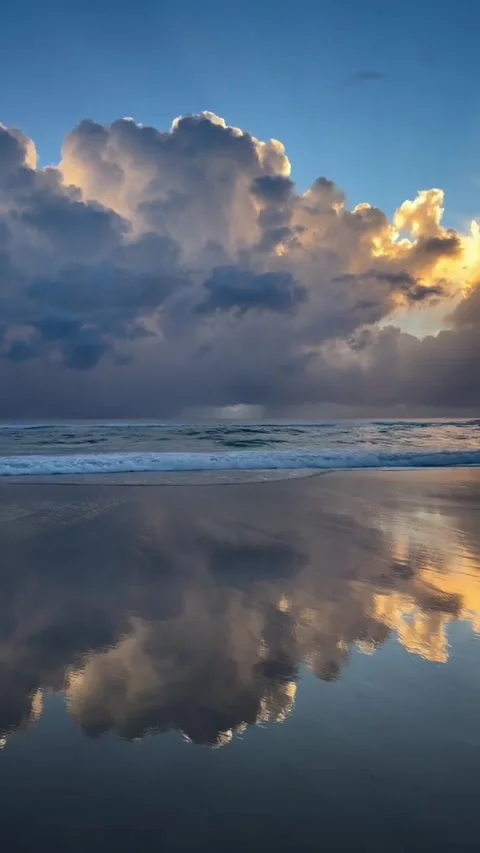 A serene beach scene at sunset with calm waters reflecting vibrant clouds in a Vidéo 333021908