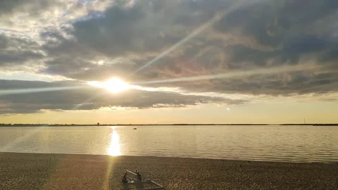 Serene beach scene at sunset, with sun casting golden glow on water. Clouds in Stockbeeldmateriaal 317982005