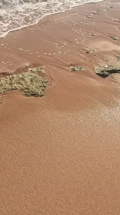 A Serene Beach Scene: Waves Gently Lapping Over Textured Rocks and Sandy 库存影片 330094779