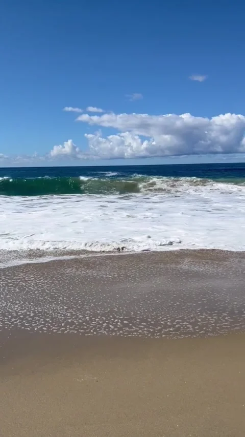 A serene beach scene with waves gently lapping at the shore under a clear blue Vídeos de archivo 333022155