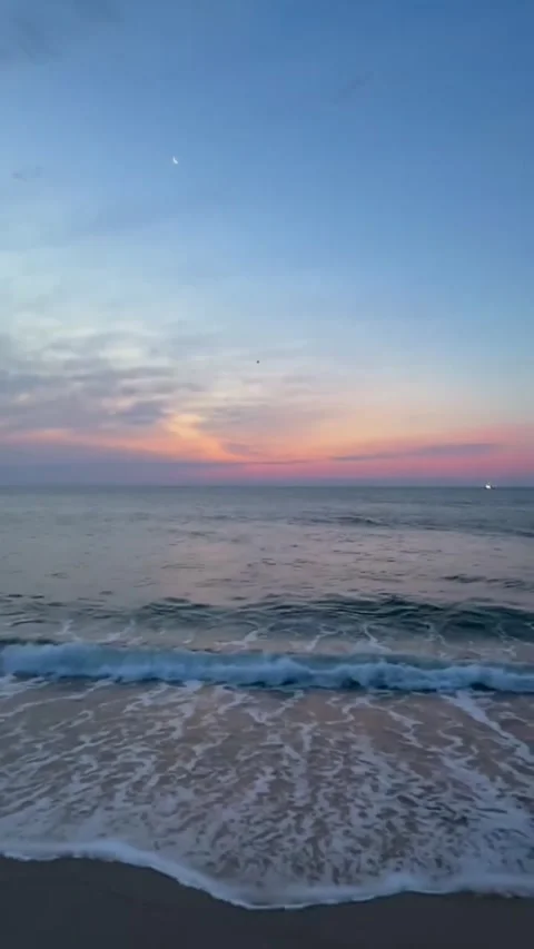Serene beach sunset with crescent moon and gentle ocean waves at twilight Stockbeeldmateriaal 334085032