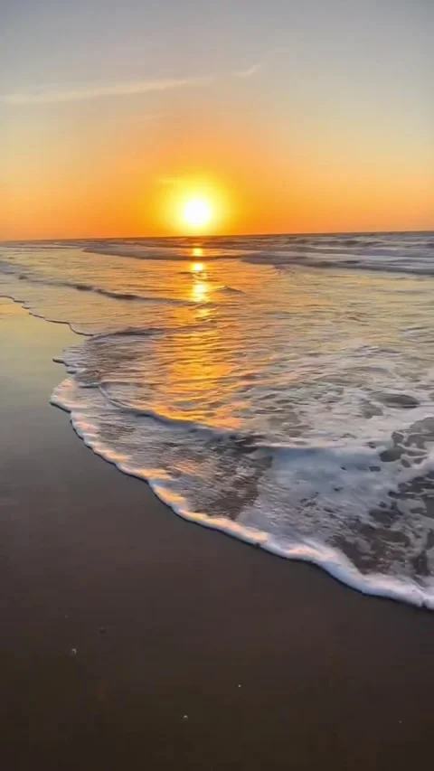 A serene beach at sunset with gentle waves lapping at the shore in a peaceful Vidéo 333021747