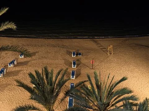 Serene beach under moonlight, tranquil shoreline with arranged loungers beneath Stock Photos