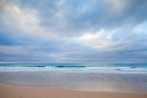 A serene beach view featuring calm waves gently lapping a sandy shore Stock Photos