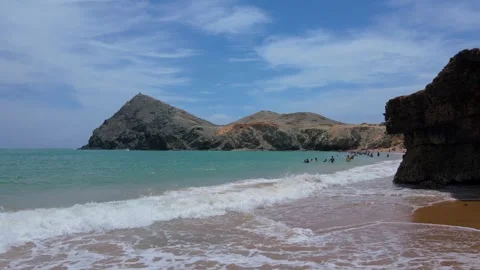 Serene beach view with gentle waves and rocky cliff Stock Footage 330380438