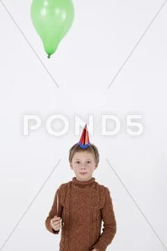 A serene boy wearing a party hat and holding a balloon, close-up Stock Photos
