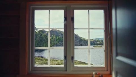 A Serene Cabin Window in Bessaker Offers a View of a Calm Lake, Surrounded by Stock Footage 334087648