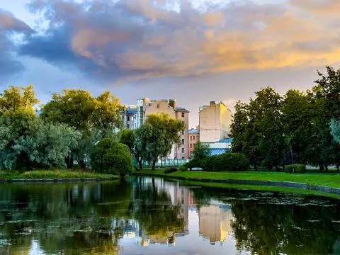 Serene Cityscape with Reflections in a Tranquil Park Pond at Sunset Stock Photos