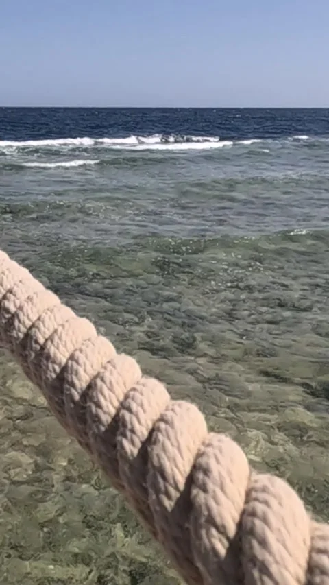 A Serene Coastal Scene Featuring Reflections of Calm Waters and a Textured Rope Stockbeeldmateriaal 330095349